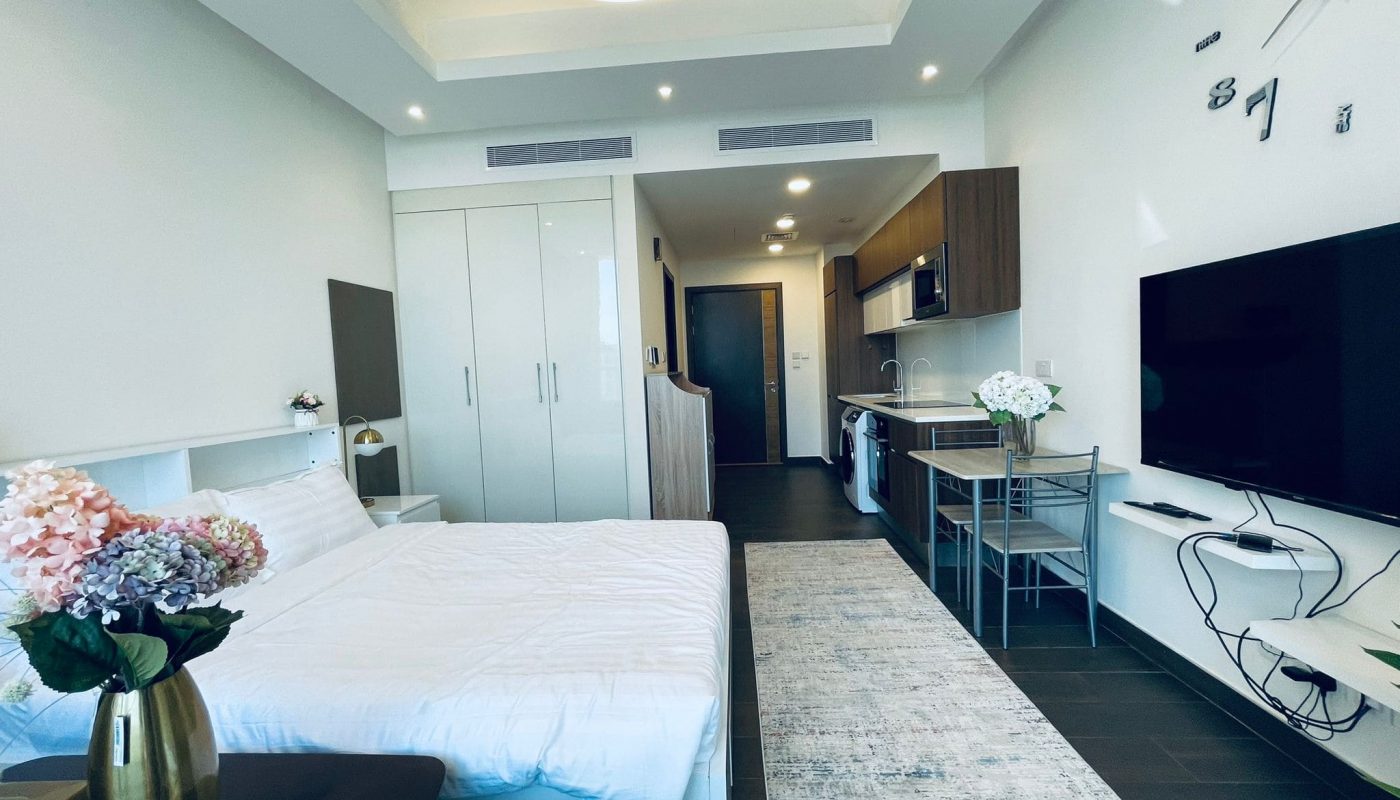 Luxury studio apartment interior with a bed, tv, kitchenette, and dining area, featuring minimalist décor and clean lines.