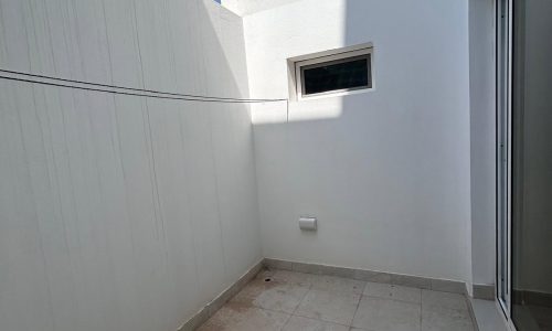 Small empty outdoor balcony with tiled floor, white walls, and an auto draft clothesline, bordered by a sliding glass door on the left.