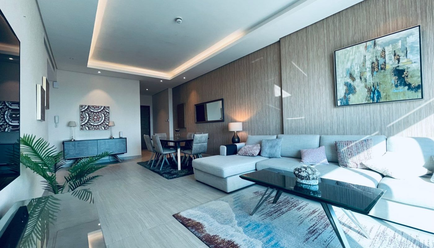 Modern living room with a gray sectional sofa, wooden walls, abstract art pieces, and a view of the adjacent dining area.