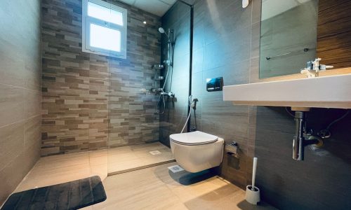 Modern bathroom with a floating toilet, glass shower area, tiled walls, and a wall-mounted sink under a small window.