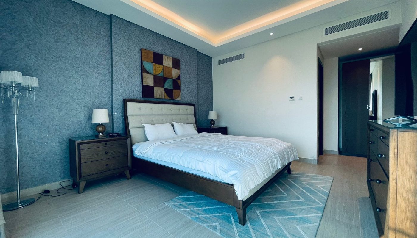 A modern bedroom with a king-sized bed, gray textured walls, and ambient ceiling lighting.