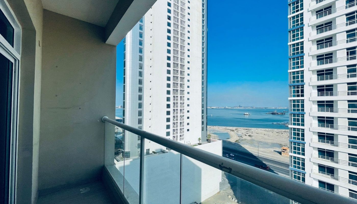 View from a high-rise balcony featuring neighboring skyscrapers and a distant ocean vista, under a clear blue sky.
