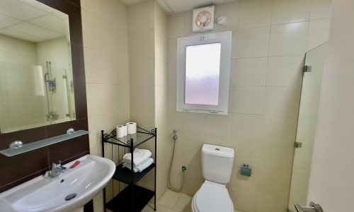 Interior of a modern bathroom featuring a toilet, sink, and shower with beige tiled walls and a towel rack.