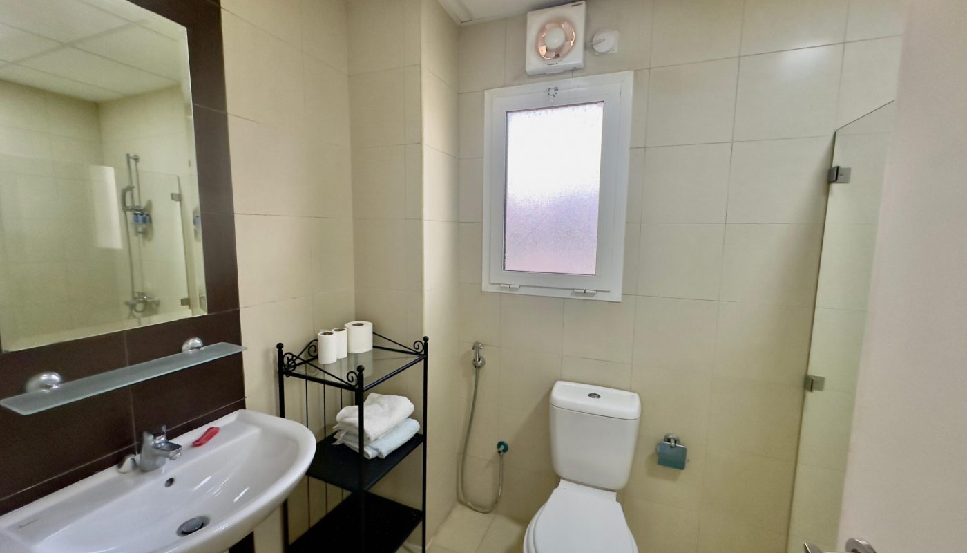 Interior of a modern bathroom featuring a toilet, sink, and shower with beige tiled walls and a towel rack.