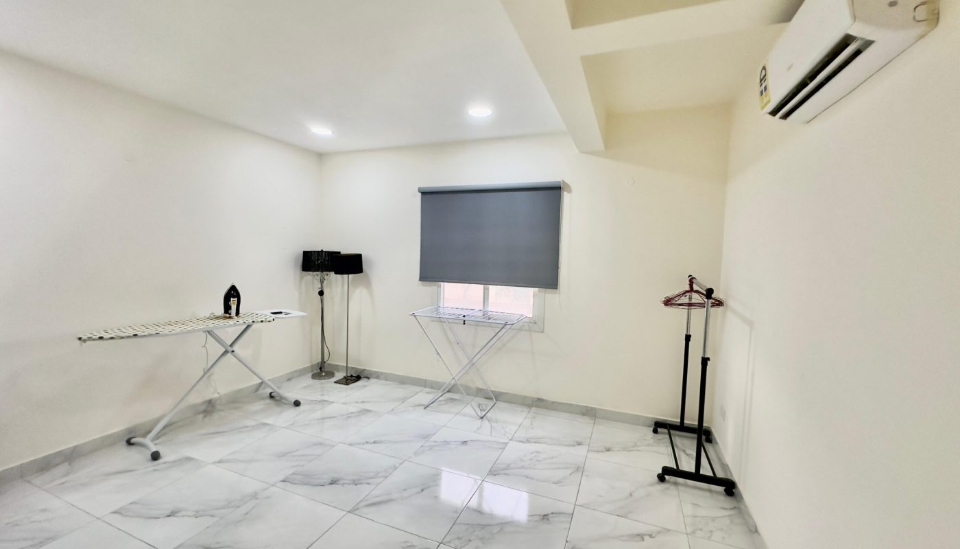 A modern, empty white room with marble floors, featuring an ironing board, projector screen, coat rack, and wall-mounted air conditioner.