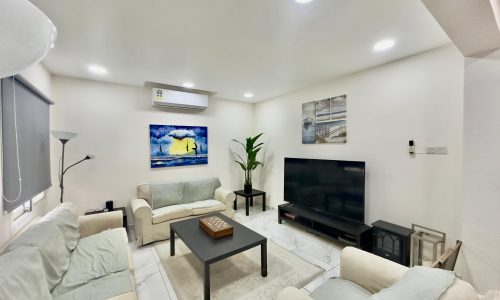 Bright living room with white walls featuring two sofas, a black coffee table, wall-mounted tv, and some landscape paintings.