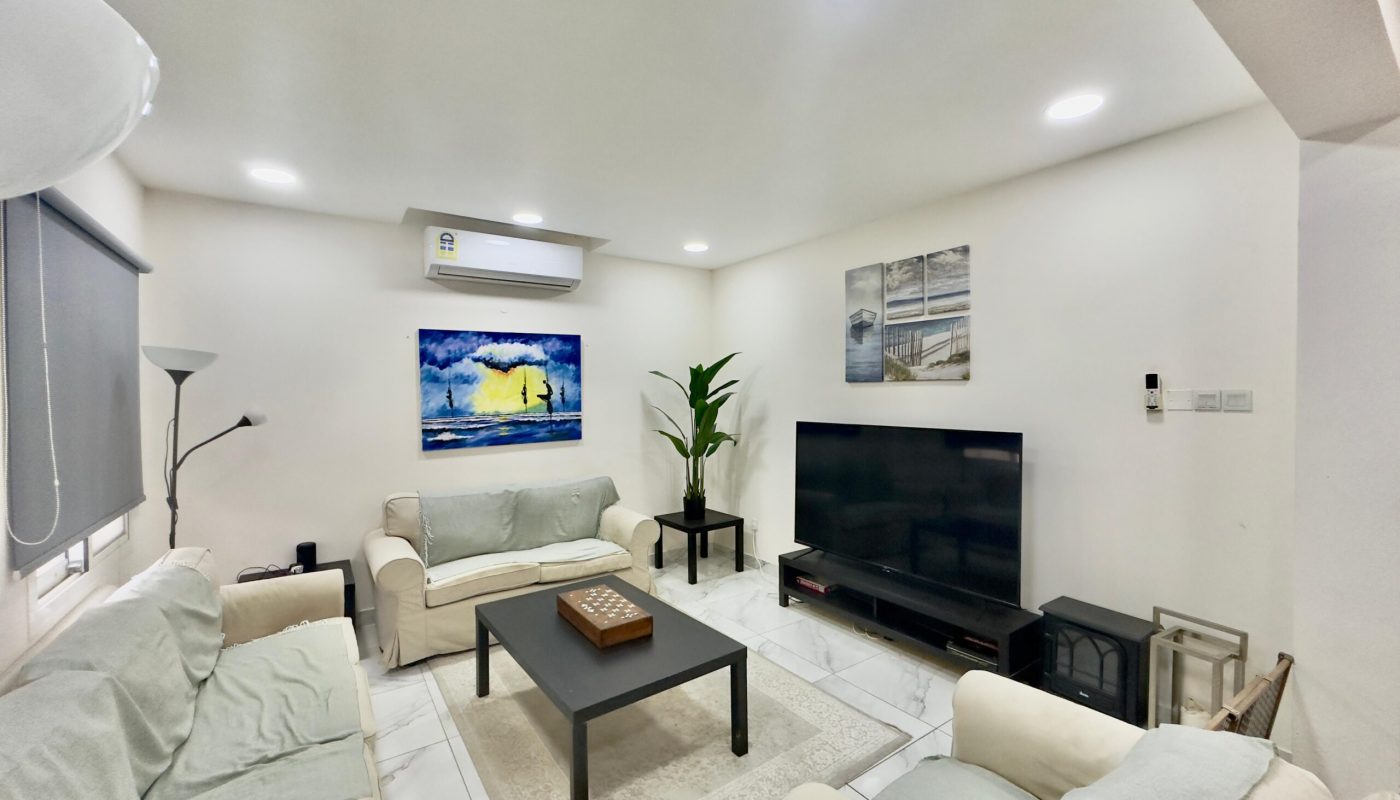 Bright living room with white walls featuring two sofas, a black coffee table, wall-mounted tv, and some landscape paintings.
