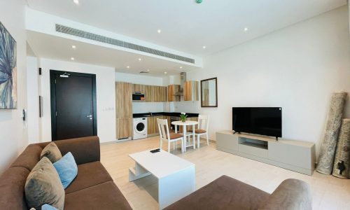 Stylish apartment interior showing a living room with a brown sofa, white coffee table, and an integrated kitchen area with appliances.