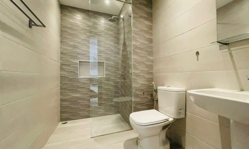 Modern bathroom interior in a stylish apartment with a glass shower enclosure, beige wavy tile walls, white toilet, and a sink.