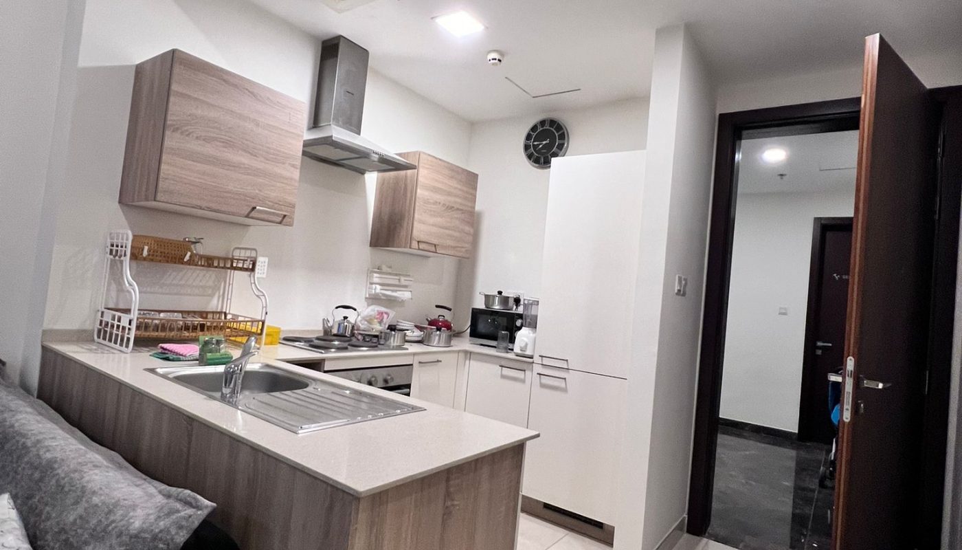 Modern kitchen interior with wooden cabinets, built-in sink, white countertops, and a visible living area entrance.