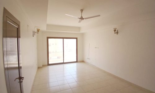 Empty, brightly lit room with white walls, tiled floor, a ceiling fan, and a glass door leading to a balcony.