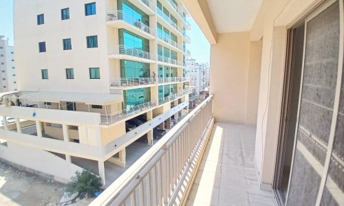 View from a sunny balcony showcasing neighboring apartment buildings and an adjacent parking structure.