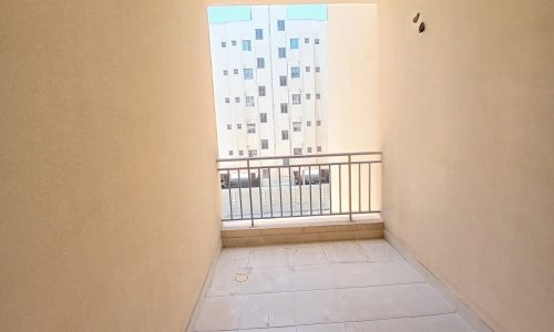 View from a bare balcony in an apartment, overlooking other buildings, with visible railing and tiled floor.