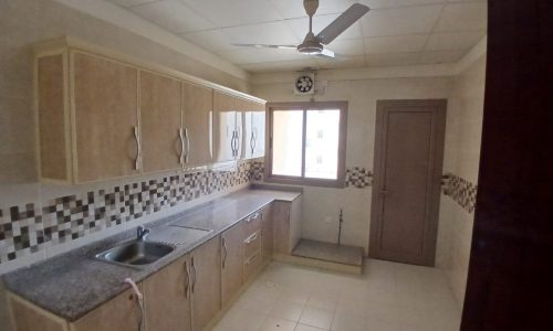 Interior of a spacious kitchen with beige cabinetry, a double sink, tiled backsplash, and a ceiling fan, with natural light from a window.