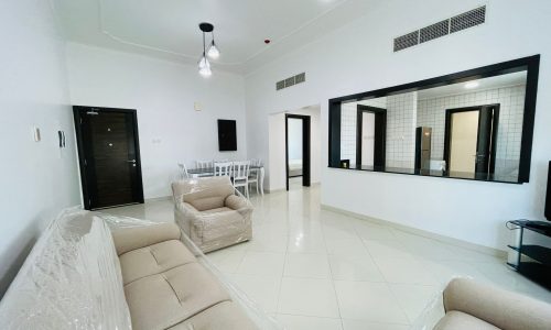 Stylish apartment living room with cream sofas covered in plastic, a dining area, large mirrors, and multiple light fixtures.