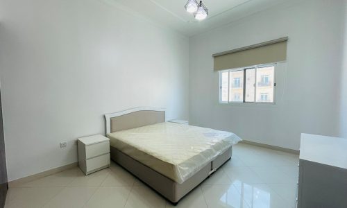 Minimalist bedroom in a stylish apartment with a double bed, white walls, tile flooring, and a large window.