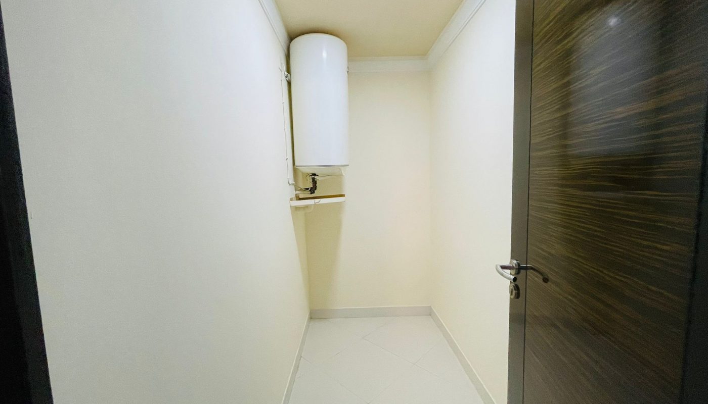 Narrow hallway in an Al Burhama apartment, featuring a water heater on the wall and closed doors on both sides.
