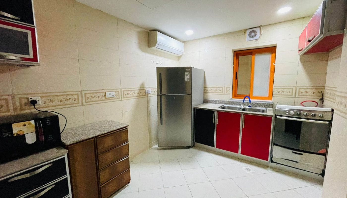 A modern kitchen in an available studio for rent, with red and black cabinets, stainless steel refrigerator, and a microwave on the counter.