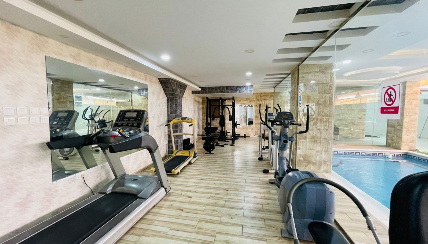 Modern indoor gym with treadmills, exercise bikes, and weight training equipment in Al Burhama, adjacent to a small swimming pool.