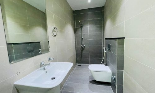 Modern bathroom in Al Burhama with a bathtub, wall-mounted toilet, sink, and shower, all set against gray tiled walls and flooring.