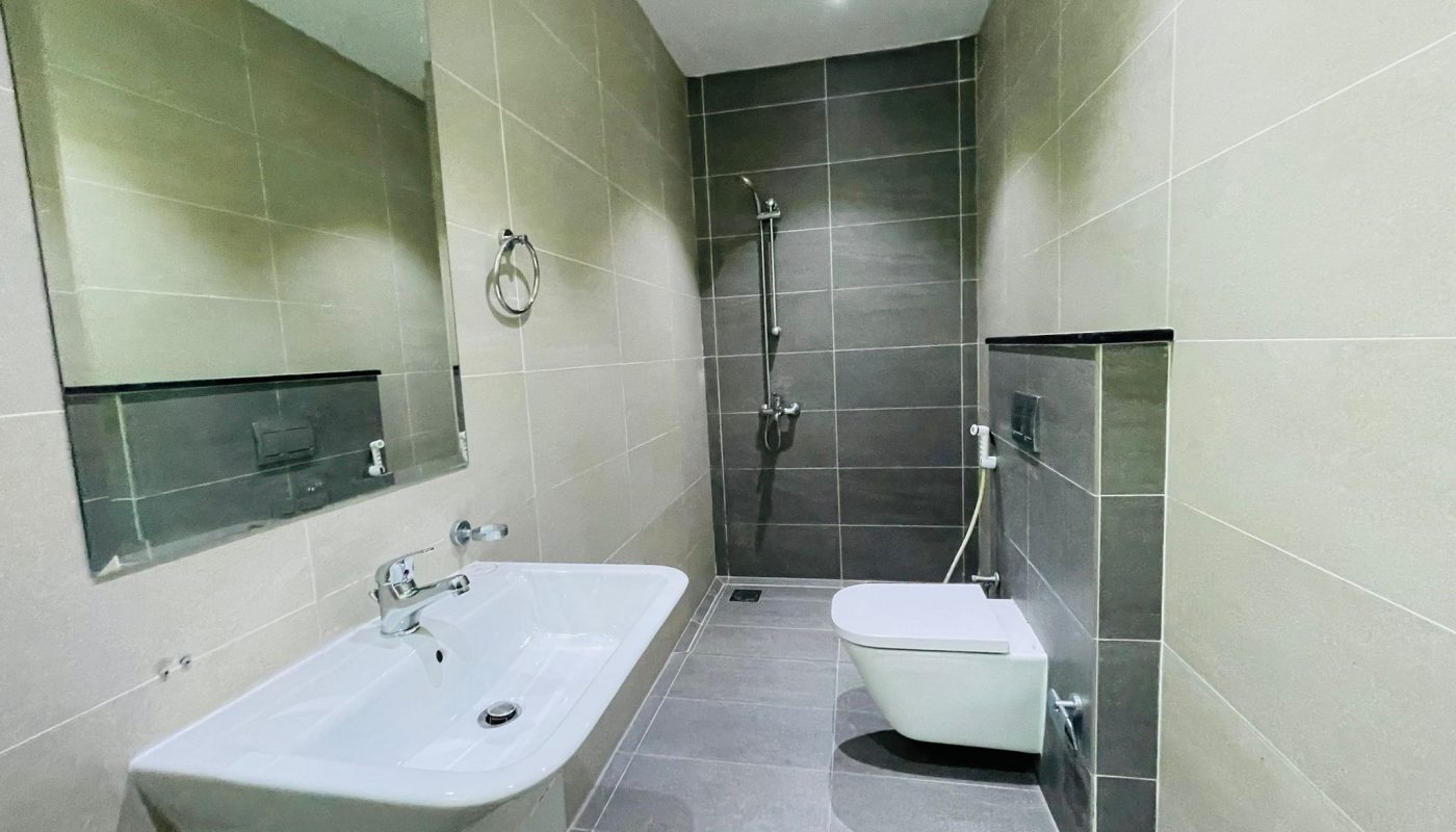 Modern bathroom in Al Burhama with a bathtub, wall-mounted toilet, sink, and shower, all set against gray tiled walls and flooring.