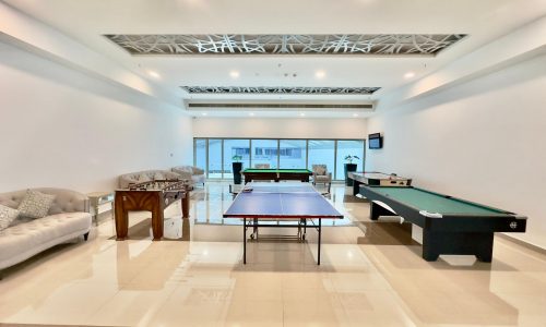 A spacious recreation room in a luxury apartment with a ping pong table, pool table, foosball table, and a comfortable seating area.