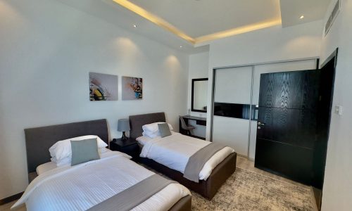 Luxury apartment room with two twin beds, a large mirror, wall art, and a flat-screen tv, featuring neutral color tones and contemporary decor.