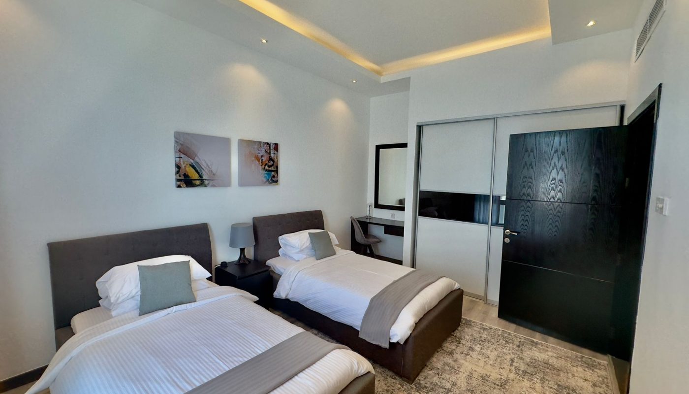 Luxury apartment room with two twin beds, a large mirror, wall art, and a flat-screen tv, featuring neutral color tones and contemporary decor.