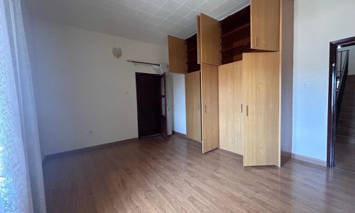 An empty room featuring wood flooring, a row of tall wooden cabinets, and doors leading to another room and the outside.