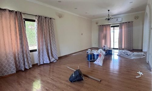 Empty living room with hardwood floors, curtained windows, and scattered renovation materials for SEO keywords optimization.