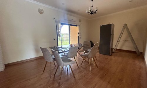 An empty dining room with a table, chairs, fridge, and a ladder against a wall, possibly indicating ongoing interior work or auto draft.