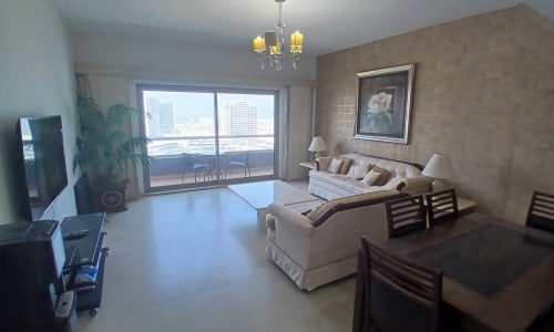 Modern flat with a beige sofa, matching armchairs, a glass door leading to a balcony with a city view. A dining area with a dark wooden table is visible on the left.