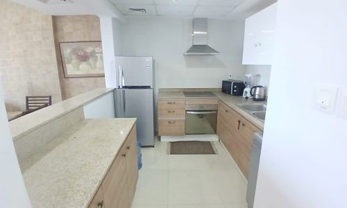 A modern flat with beige countertops, wooden cabinets, stainless steel appliances, and a tiled backsplash in Amwaj.