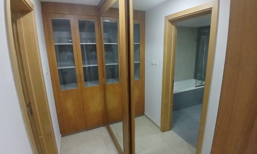 Interior of a modern flat's hallway with wooden doors and a mirrored cabinet reflecting an open bathroom door.