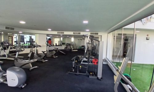 A modern gym in Amwaj with various workout machines, including treadmills and weight stations, and an area with artificial turf.