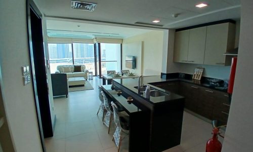 Modern kitchen with a black island, leading to an open-plan living area with large windows overlooking a cityscape and an auto draft system.