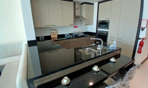 A modern kitchen with beige cabinets, black countertops, and built-in appliances. An auto draft breakfast bar with two stools is visible, and there is a red fire extinguisher to the right.