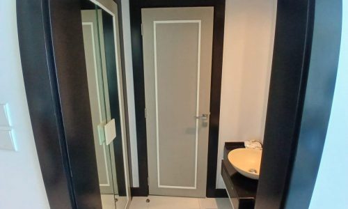 Interior view of an auto draft bathroom with a white door open, revealing a sink and mirror, framed by dark doorways and reflective surfaces.