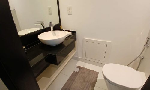 Modern bathroom with black countertop, white vessel sink, mirror, auto draft, and a toilet next to a gray bath mat.