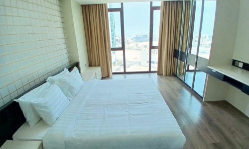 Modern hotel room with large bed, floor-to-ceiling windows, city view, and auto draft beige curtains.