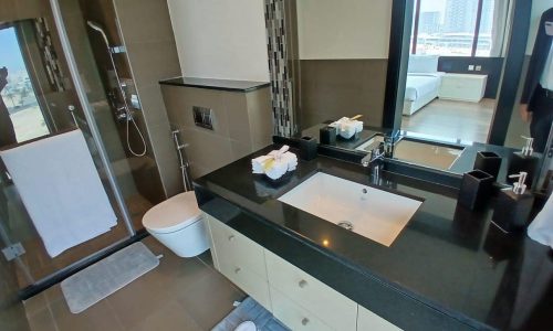 Modern hotel bathroom with large mirror, double sink vanity, walk-in shower, and city view through a floor-to-ceiling Auto Draft.