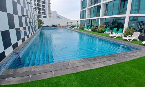 Outdoor swimming pool with loungers, bordered by high-rise buildings and artificial grass in an auto draft urban setting.