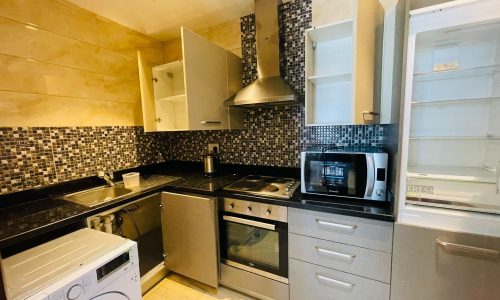 Modern kitchen with stainless steel appliances, mosaic tile backsplash, and a combination of dark countertops and grey cabinets.