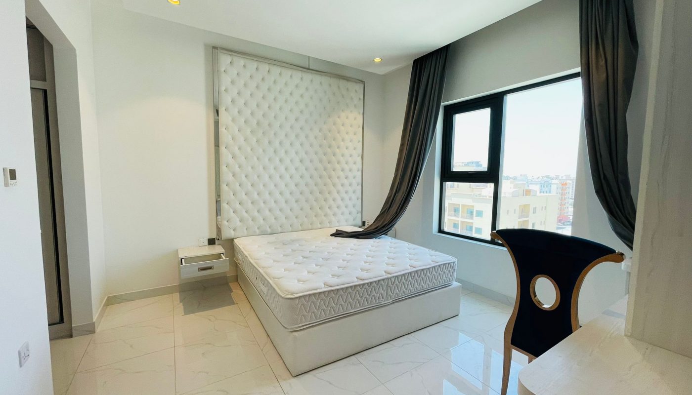 Modern bedroom with a large tufted headboard, king-sized bed, sleek black chair, and expansive window with curtains.