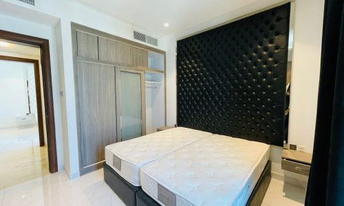 Modern bedroom with a large bed featuring a white mattress and a black tufted headboard, mirrored wardrobe, and wooden door.