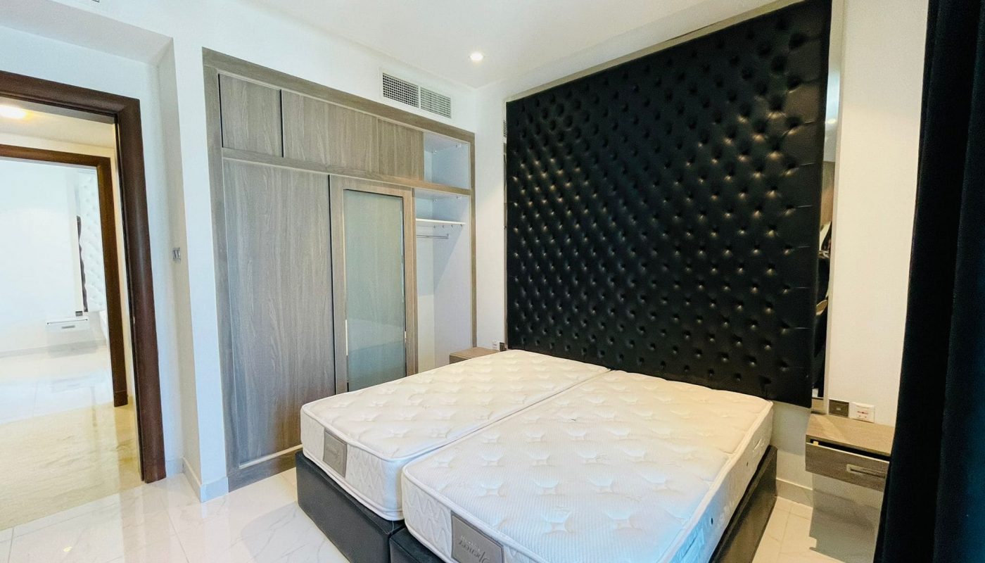 Modern bedroom with a large bed featuring a white mattress and a black tufted headboard, mirrored wardrobe, and wooden door.