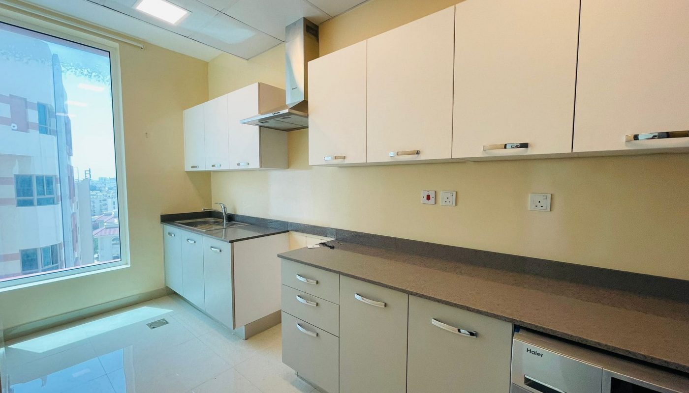 Modern kitchen in a luxury apartment with beige cabinets, dark countertops, and built-in appliances, featuring a window with a city view.