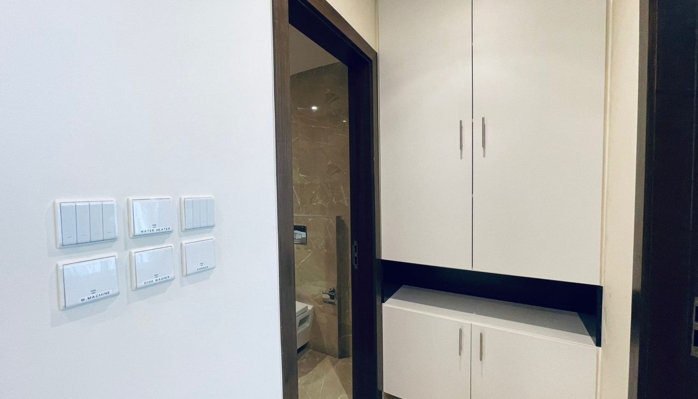A modern bathroom entrance with open door, showcasing a wall of light switches and a white cabinet.