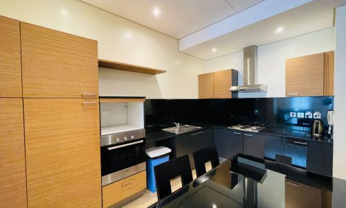 Luxury apartment kitchen interior with light wood cabinets, black countertops, and built-in appliances.