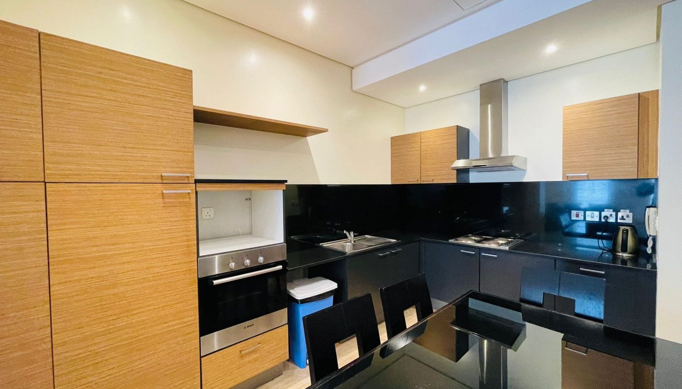 Luxury apartment kitchen interior with light wood cabinets, black countertops, and built-in appliances.